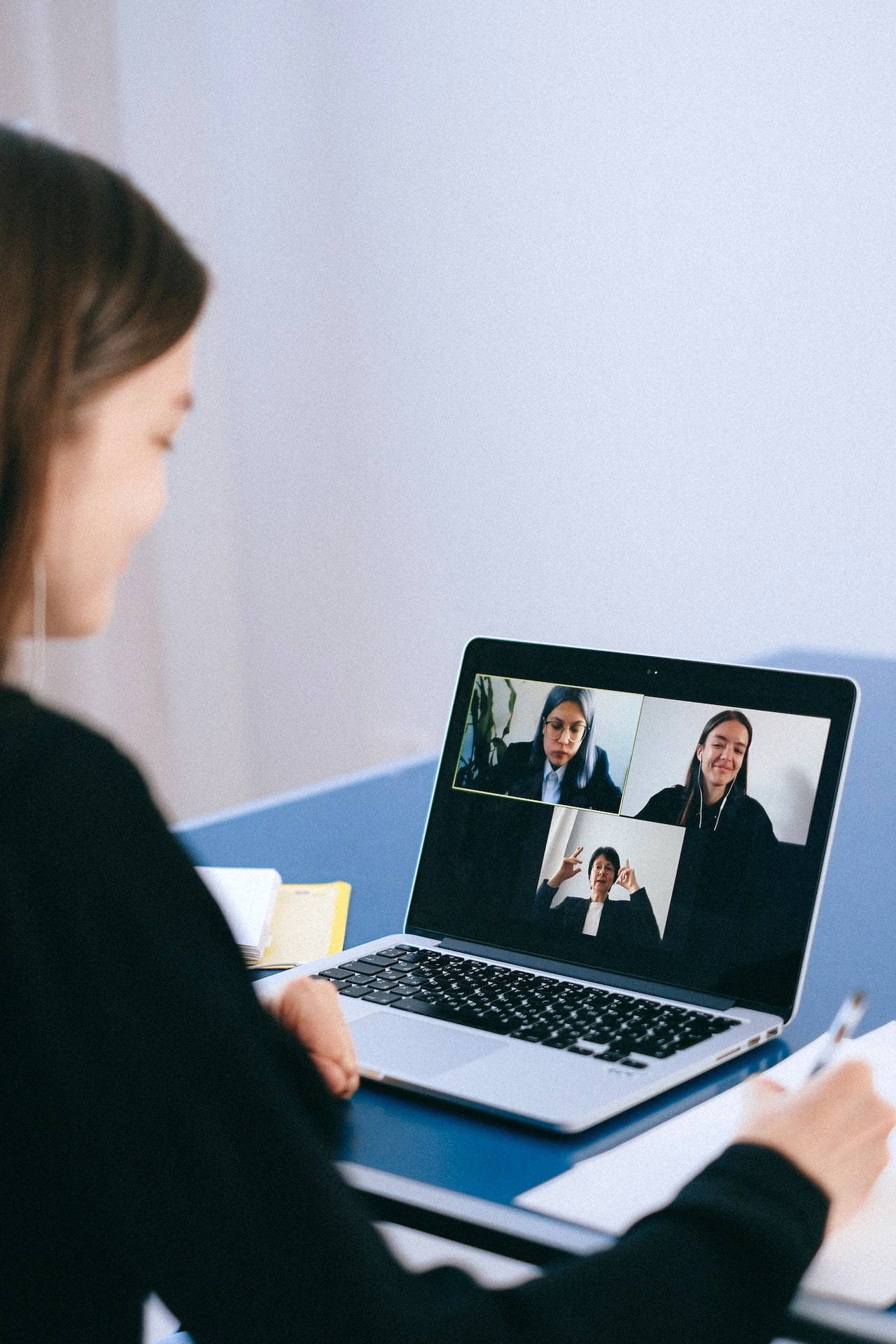 business woman sitting in front of a laptop showing a video call with another person while taking notes on her legal pad.